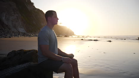 Un-Joven-Fuerte-En-Silueta-Sentado-En-Una-Pose-De-Meditación-Para-Liberar-El-Estrés-Y-Entrenar-La-Atención-Y-La-Positividad-Al-Amanecer-En-Santa-Barbara,-California-A-Cámara-Lenta