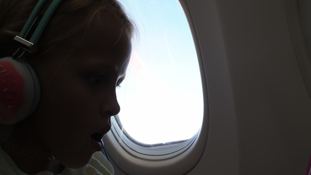 Child Looking Out Airplane Window with Donut Headphones