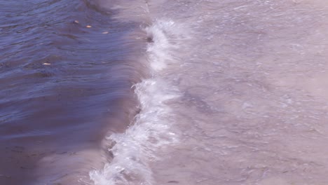 Nahaufnahme-Der-Wellen,-Die-Tagsüber-Am-Strand-Rollen-Und-Den-Himmel-Auf-Der-Wasseroberfläche-Reflektieren