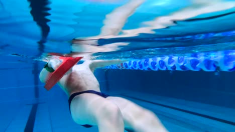 niño joven activo nadando paleta de espalda en piscina pública en el interior
