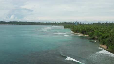 Aerial-flight-above-breaking-waves-on-turquoise-Indonesian-palm-beach-bay