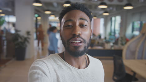 Portrait-Of-Young-Businessman-Vlogging-Into-Camera-In-Modern-Open-Plan-Office