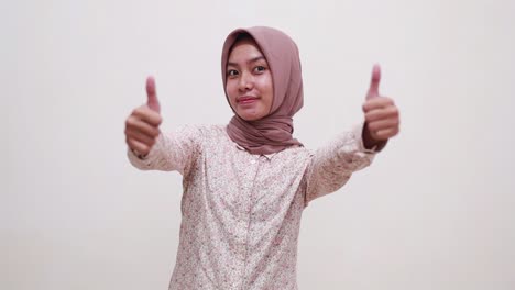 cheerful young asian muslim girl standing while showing thumbs up