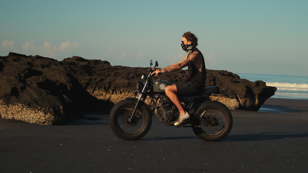 hombre montando una motocicleta en una playa al atardecer