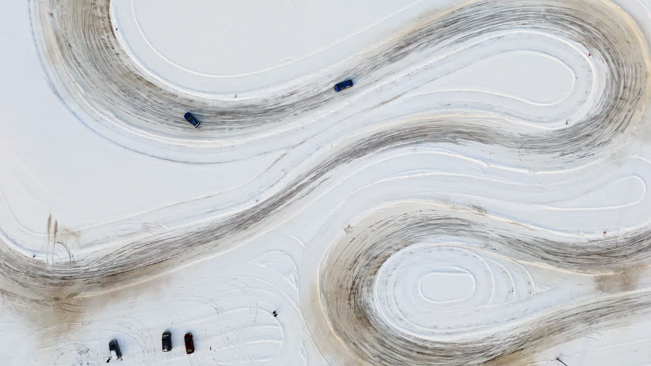 Cenital aerial view following cars racing on a ice track, sunny, winter day