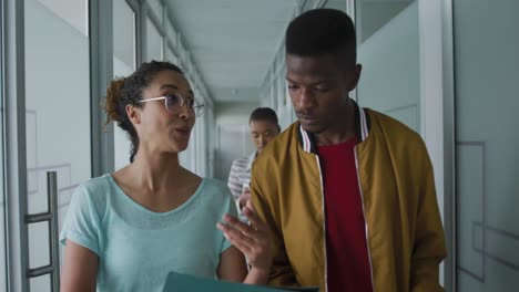 happy diverse male and female creative colleague walking in workplace corridor and talking