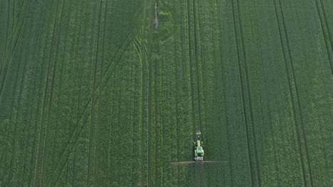 vertical aerial as tractor spraying crop field enters bottom of frame