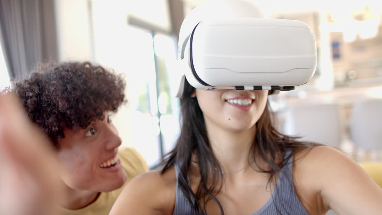 Using VR headset, woman enjoying virtual reality with excited friend nearby