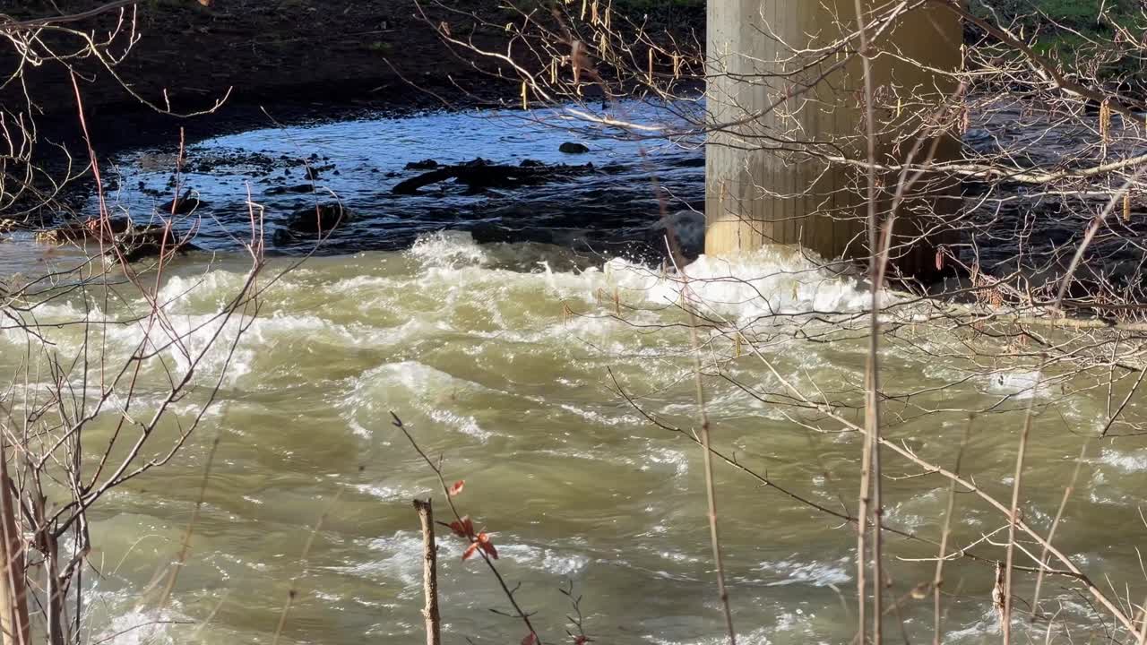 Schnell fließender Fluss mit starker Strömung unter einer Brücke im Winter.