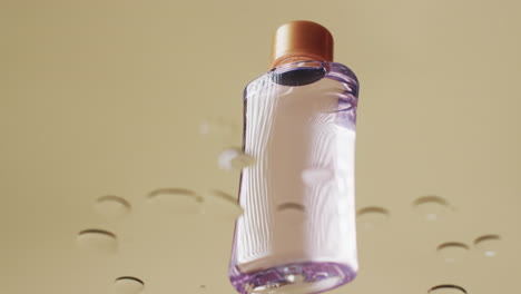 video of beauty product bottle in water with copy space on yellow background