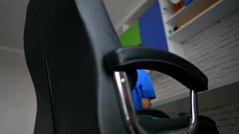 cute toddler boy sits in a office chair with phone in hands. barefoot kid is rotated in the chair. low angle view.