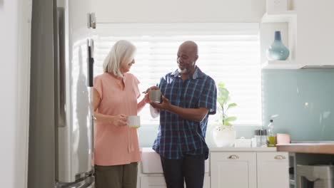 happy senior diverse couple drinking coffee in kitchen