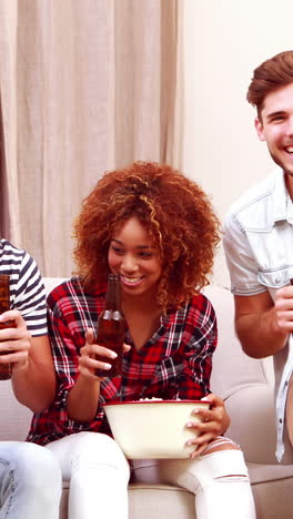 smiling friends watching tv while eating popcorn and drinking beer