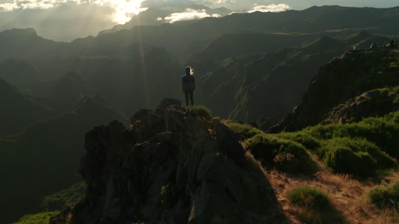 Young woman stands on cliff watching bright sunrise with beautiful landscape