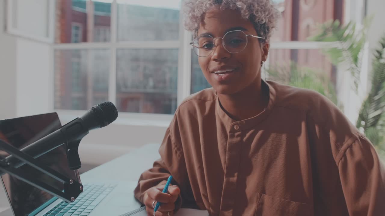 Young african american woman radio host in headphones sits at desk with laptop