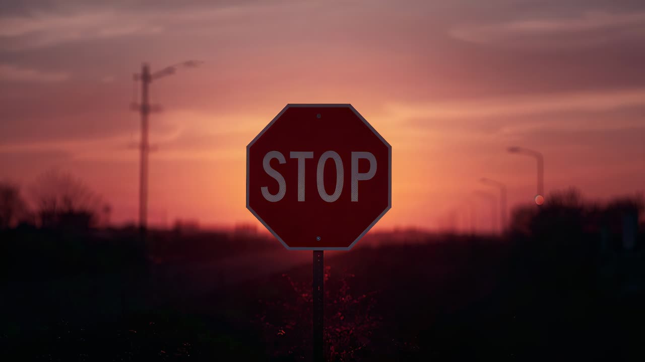 Framing centered red octagon STOP sign glowing as low sun emerging over roadside, with utility pole