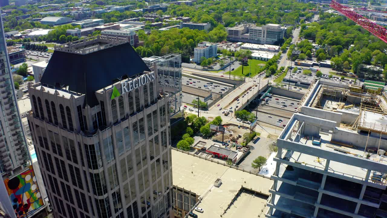 un dron aéreo disparado muy lentamente descendiendo mirando más allá de la torre del banco de las regiones y otro sitio de construcción en la concurrida autopista en el centro de atlanta, georgia en un día soleado