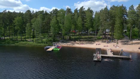 people play and jump off of dock swimming in alpine lake below forest in sweden