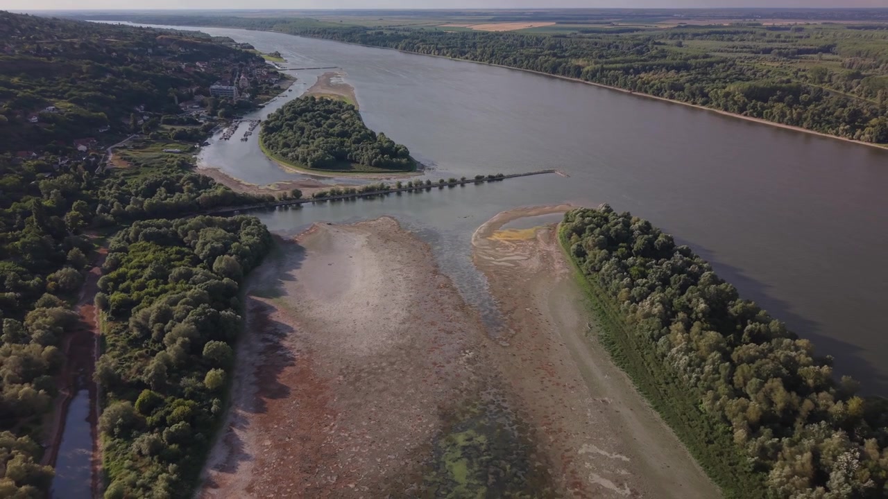 Vista aerea con drone del fiume Danubio durante la siccità. Ampie aree di letto del fiume asciutto e crepato e piane di fango sono esposte a causa dei livelli d'acqua estremamente bassi, con sponde alberate e un cielo nuvoloso