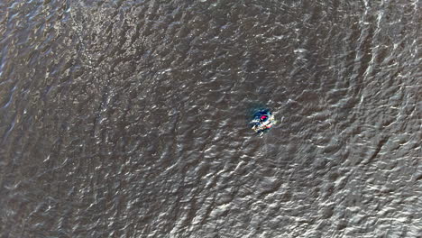 from a steady overhead drone, a lone diver swims beside a bright marker buoy on textured open water, suggesting training, alert awareness, and measured endurance in a minimalist scene