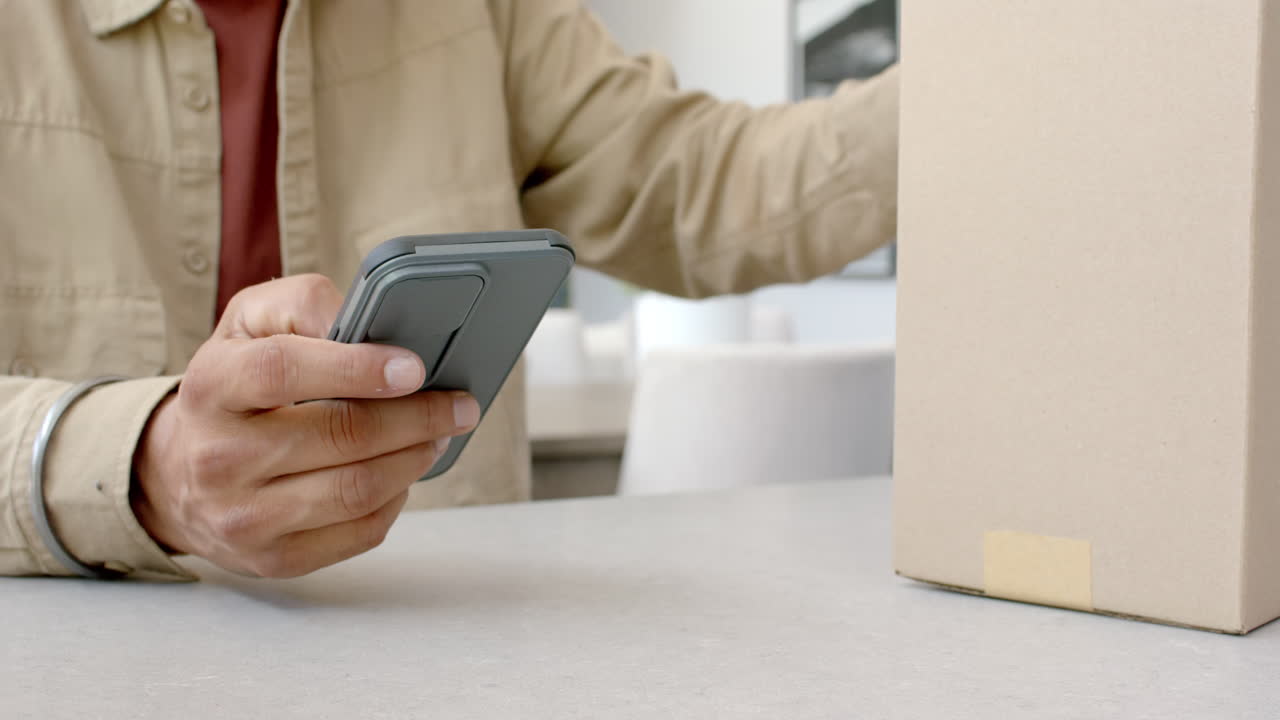 Holding smartphone, man checking package delivery status at home table