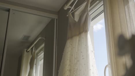 beautiful elegant wedding dress hanging on window.