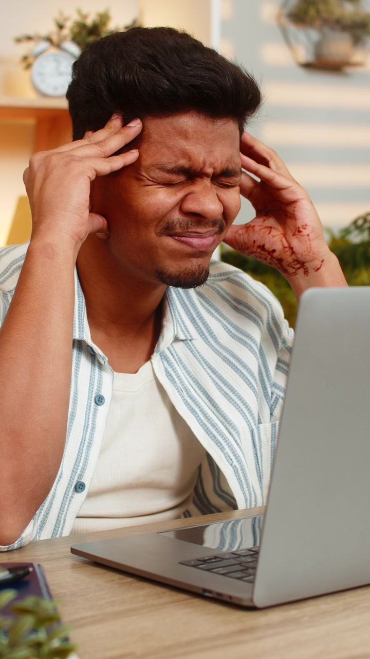 Indian man on home table looking at laptop screen and thinking seriously during focused remote work