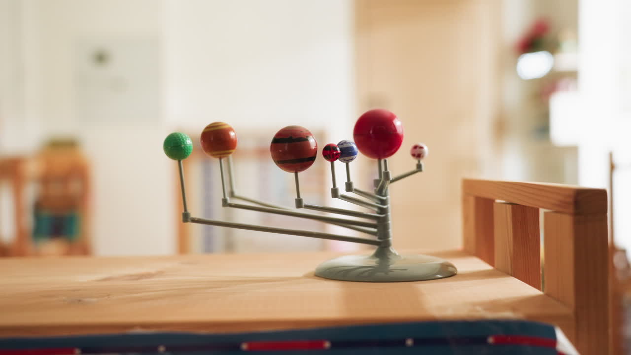 Close up of colorful nine planet educational model placed on wooden surface under warm indoor lighting, showcasing miniature solar system structure used for classroom learning