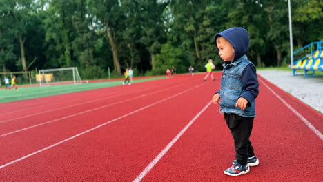focused caucasian boy stands at the stadium. kid watches the children playing sports games.