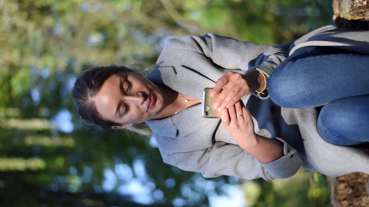 Brunette woman texting on her phone in the park. Vertical