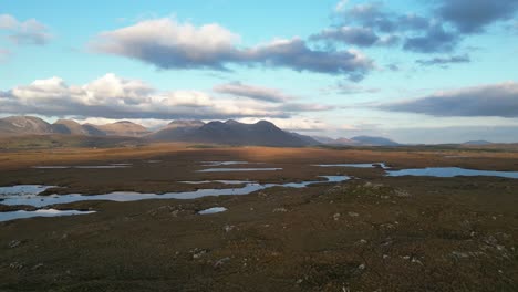 Wide-drone-shot-of-Connemara-Lakes-with-calm-lakes-in-the-foreground-and-Beanna-Beola-mountain-range-in-the-distance,-slowly-ascending-aerial-shot