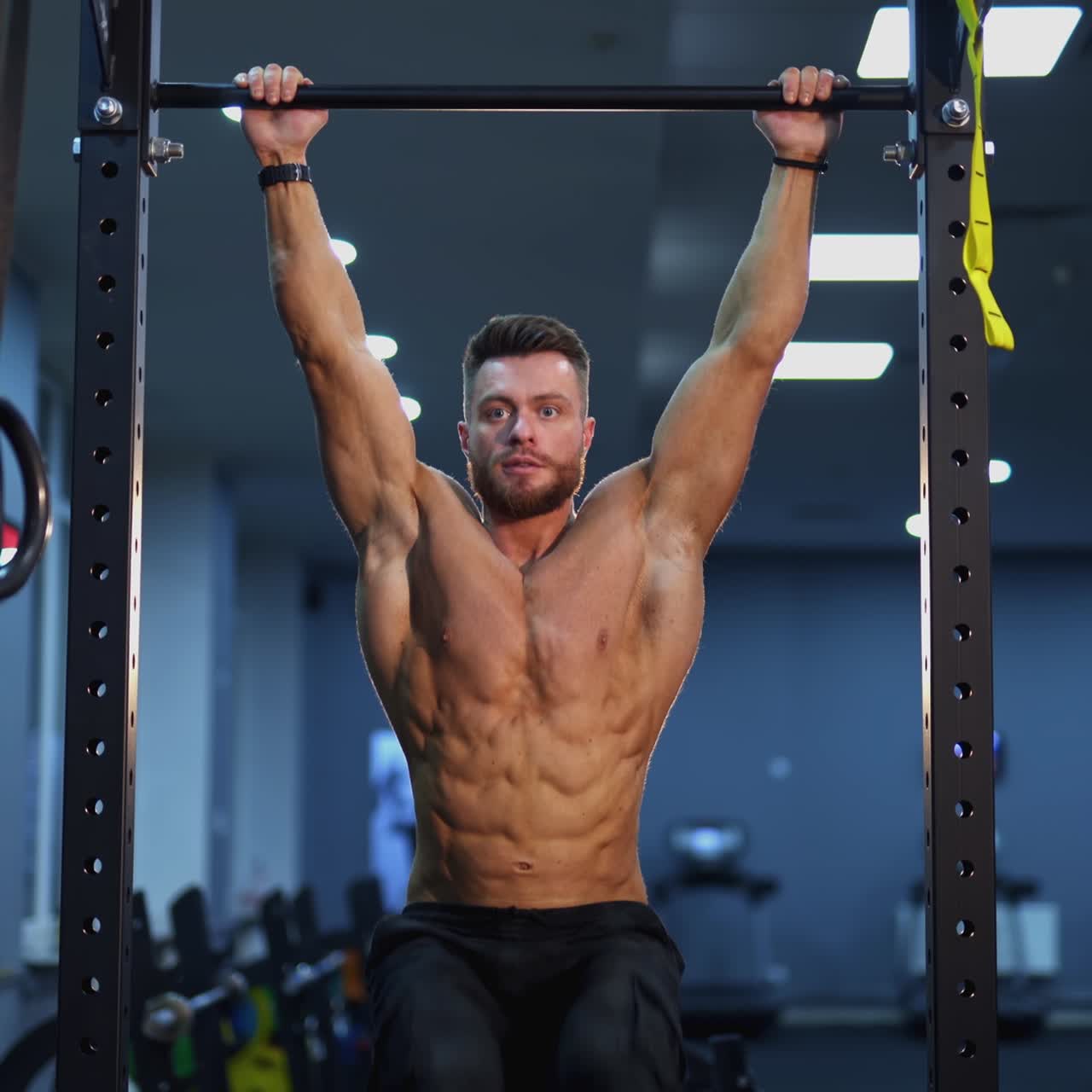 Shirtless man training on a crossbar. Portrait of a professional athlete doing exercise with tightening his legs in the gym. Everyday workout routine