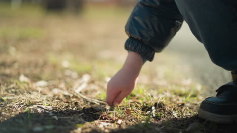 la mano de un niño joven, con una chaqueta de cuero, vaqueros y botas, mientras recoge un palo para cavar en el suelo, el palo se rompe, y después de intentarlo de nuevo, lo arroja en ira