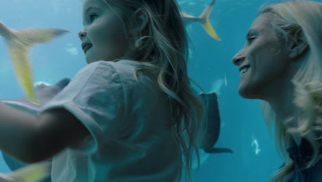 happy girl with mother at aquarium looking at stingray swimming with fish in tank child watching marine animals with curiosity having fun learning about marine life with mom in oceanarium