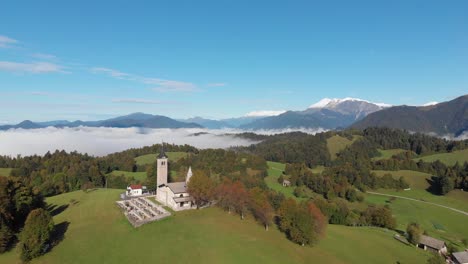 drone flying towards famous slovenian church green hills and fog in background