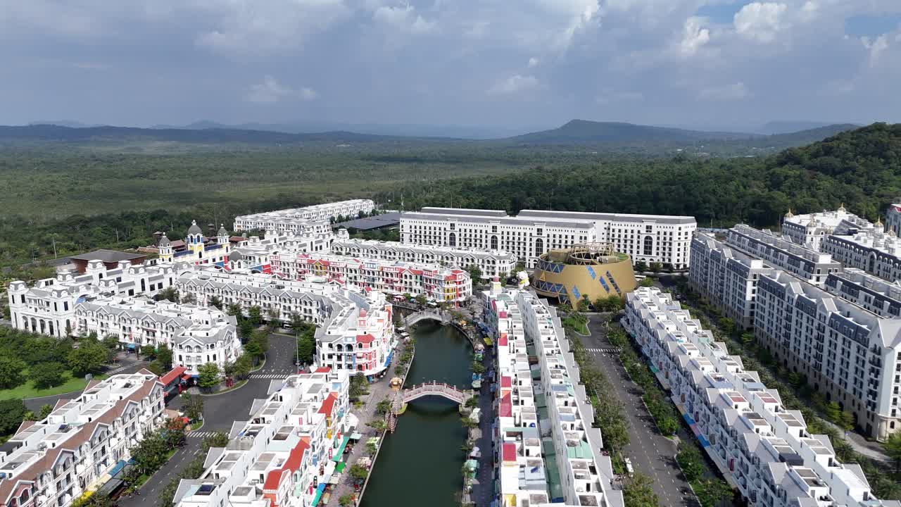 Aerial video reveals a newly built, planned urban community with a distinct architectural style with rows of colorful buildings lining a narrow waterway, designed for tourism. Man made canal system