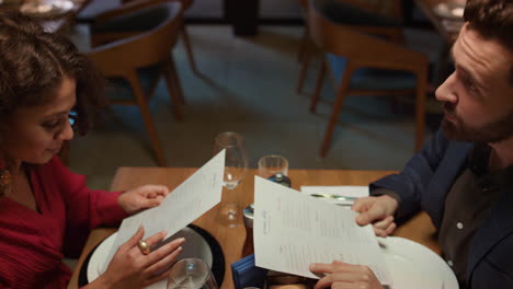 una pareja multiétnica busca un menú en un restaurante de lujo en el loft.