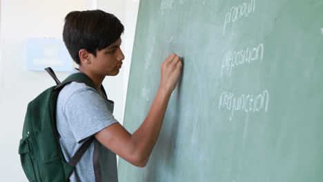 schoolboy writing on green chalkboard in classroom