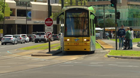 an adelaide tram pulls up at a tram stop in the city, with cars and buses driving by in the background. this video showcases a slice of everyday life in adelaide, australia.