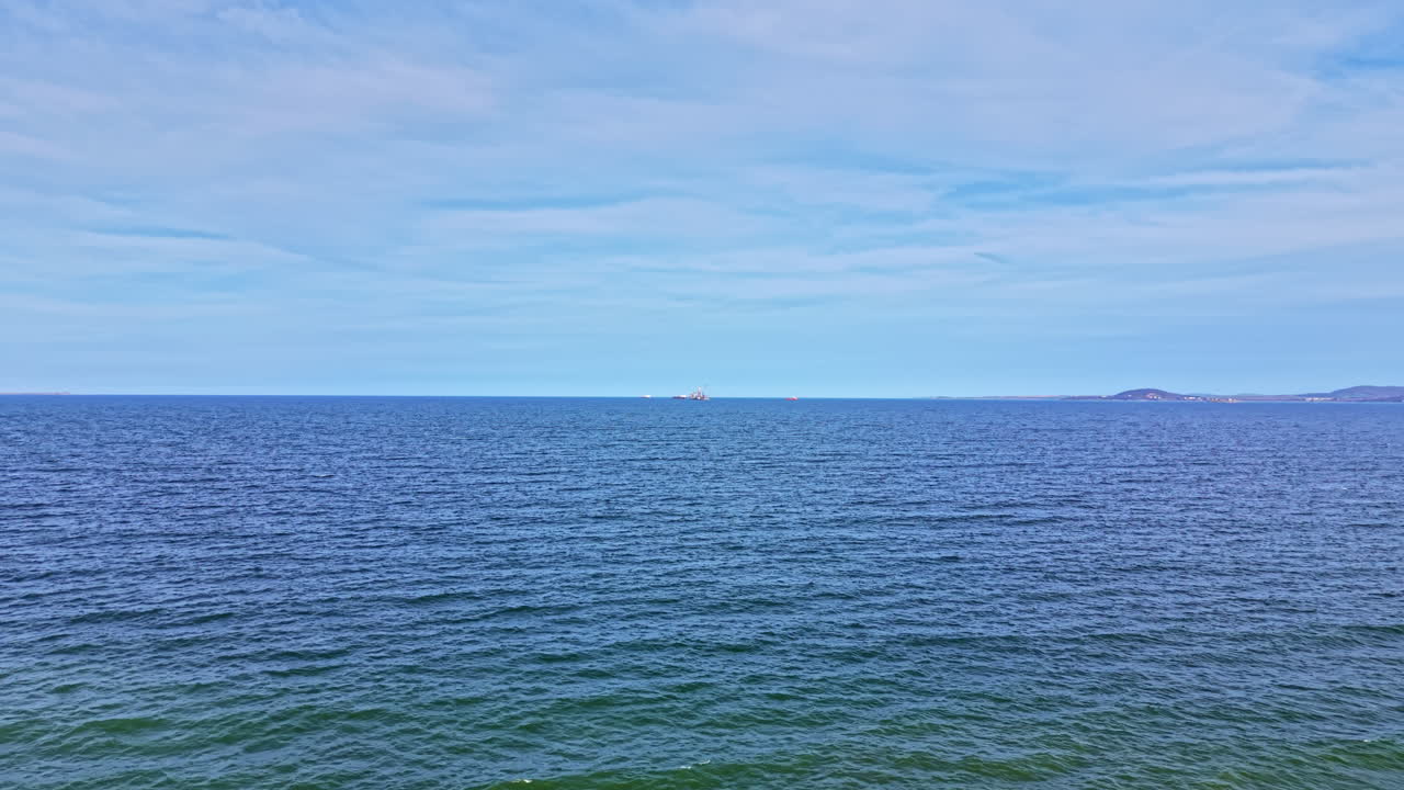 Bølger bevæger sig blidt i havet, mens et skib flyder langt ude i horisonten på en dag med klar himmel