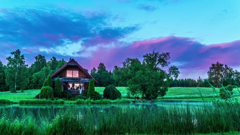 time lapse of illuminated clouds flying over charming wooden cottage on pond
