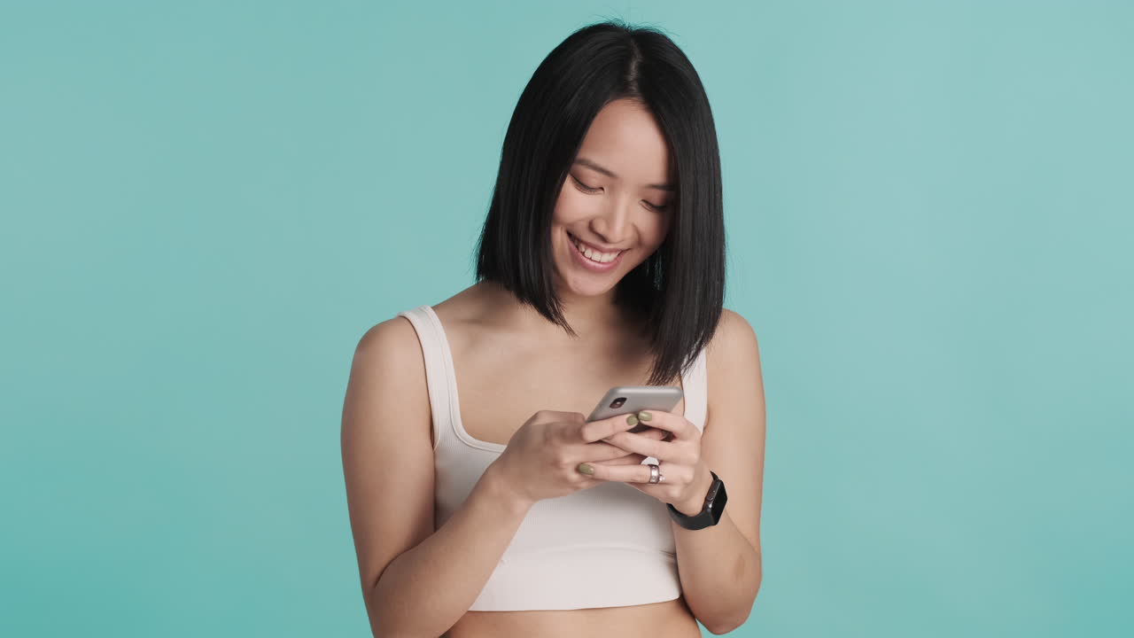Asian woman texting on smartphone and smiling.