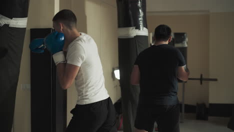 couple of male friends engaged in boxing with boxing gloves hitting punching bags with force. exercising together and improving endurance in sports club