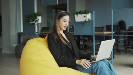 una encantadora mujer joven con ropa de negocios se sienta con su portátil en una elegante y moderna oficina de coworking, se saluda a través de una llamada de video a través de la portátil, y comienza una conversación