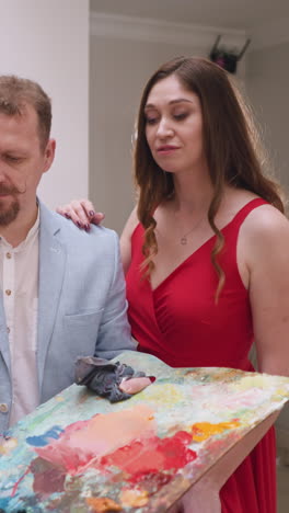 mujer se apoya en el hombro del artista en el estudio. socialite lánguida en vestido rojo abraza al maestro de arte dibujando a la dama pintando en el taller de arte. la musa inspira al pintor