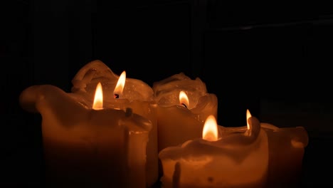 Static-video-orange-lit-candle,-slow-motion-fire-and-group-of-candles-on-black-background