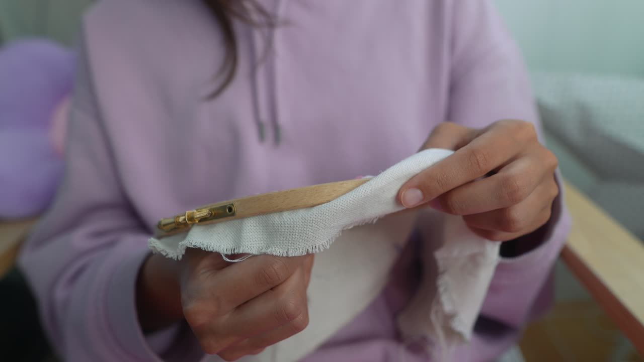 Nahaufnahme von Händen, die Stoff mit Nadel und Faden besticken