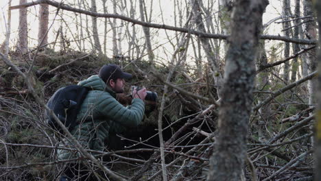 nature photographer crouching to take a photo from behind trees