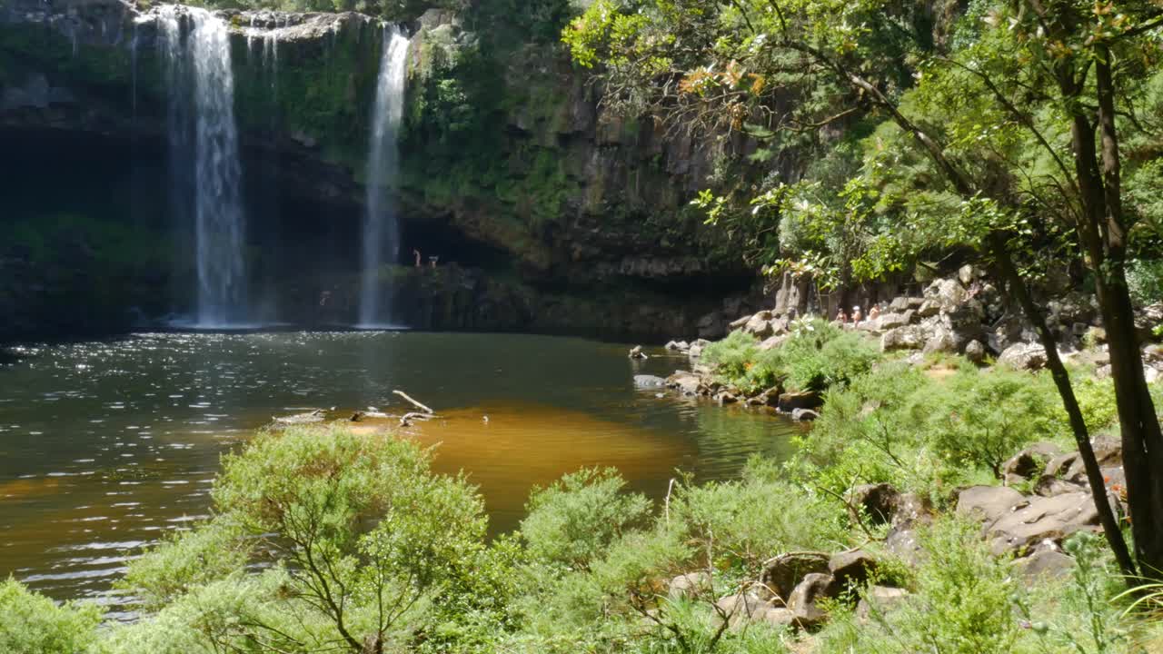 Wide shot of Kerikeri Waterfall witjh natural pond in jungle during summertime -Children having fun and jumping into water