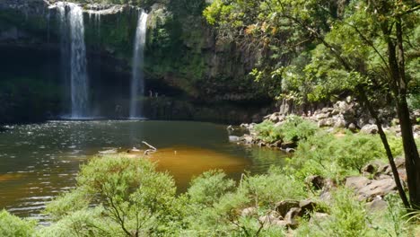 wide shot of kerikeri waterfall witjh natural pond in jungle during summertime -children having fun and jumping into water